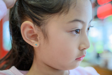 Adorable little Asian girl having ear piercing process.