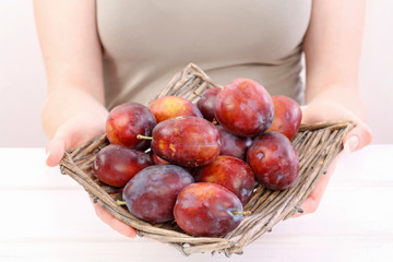 Woman holds wicker basket with ripe plums.