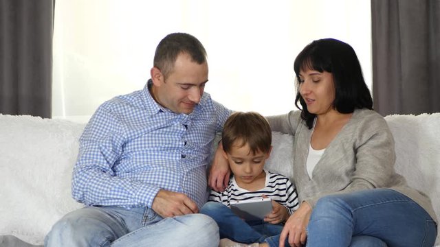 Happy family: father, mother and son use tablet while sitting on sofa. Parents and child have fun using the gadget.