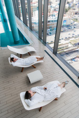 Two young man lies on a lounger in a swimming pool in a white terry dressing gown and relaxing