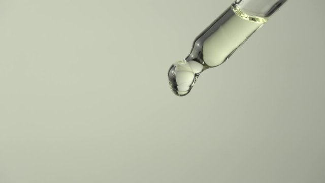 Close up of liquid oil drop from lab pipette on white background. Closeup of lavender extract droplets are falling from glass pipette.