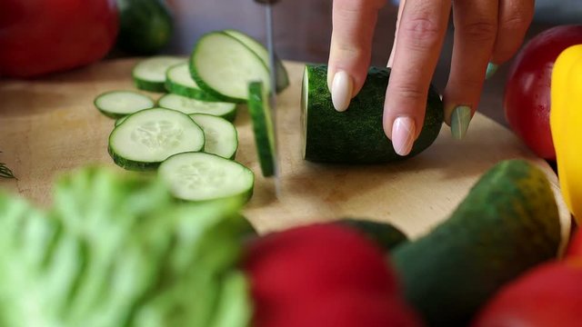 Close-up of cook cutting fresh cucumber on wooden chopping Board, slow motion. Cooking vegetable salad at home in the kitchen.