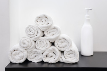 Fototapeta na wymiar Rolled up white towels with cosmetic bottle. Soap bottle and white towels rolled on a table for spa.
