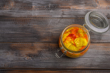 Homemade pickled cabbage leaves and pepper and carrots in a glass jar with an open lid on a wooden brown background. Rustic style