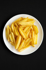 Homemade french fries on a white plate on a black background, top view. Flat lay, overhead, from above. Close-up.