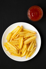 Homemade french fries with sour-sweet sauce on a white plate on a black surface, top view. Flat lay, overhead, from above.