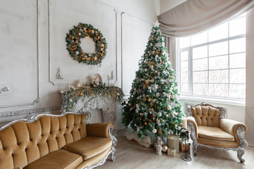 Christmas morning in classic apartments with a white fireplace, decorated tree, sofa, large windows and chandelier.