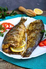 Baked herring with lemon and spices on a white plate on a wooden table. Tasty fish dish. Top view.