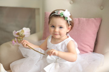 beautiful baby girl in a white dress holds a magnolia in her hand