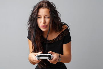 Young pretty woman playing with console joystick over a gray background.