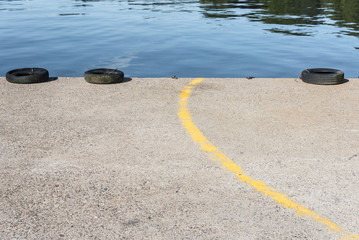 une ligne jaune sur un quai avec des pneus de voiture. Une route en bord de rivière. Des pneus et une ligne jaune sur une route au bord de l'eau. La route menant à la rivière.