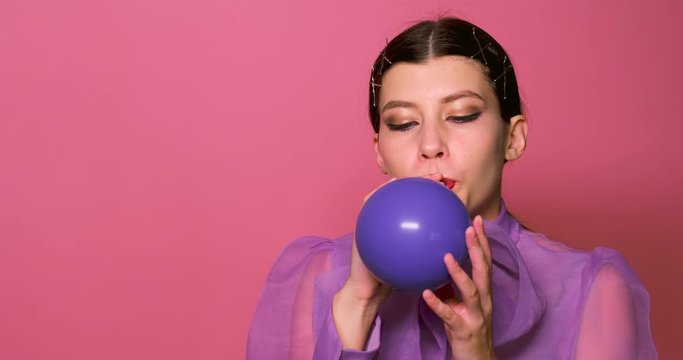 a girl inflates a purple balloon . pink background photo Studio.slow motion. girl enjoys inflating the ball. holiday concept