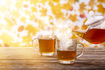 Tea is poured into a glass cup on dark wooden table, autumn background