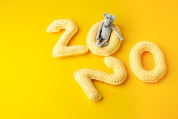 Happy New Year 2020. Number 2020 knitted from yarn and gray toy mouse symbol of year on bright yellow background, cheese color. Flat lay, top view, copy space