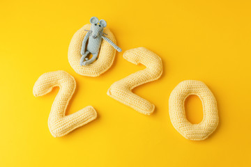 Happy New Year 2020. Number 2020 knitted from yarn and gray toy mouse symbol of year on bright yellow background, cheese color. Flat lay, top view, copy space