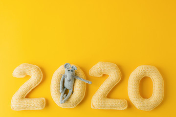 Happy New Year 2020. Number 2020 knitted from yarn and gray toy mouse symbol of year on bright yellow background, cheese color. Flat lay, top view, copy space