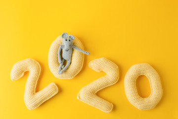 Happy New Year 2020. Number 2020 knitted from yarn and gray toy mouse symbol of year on bright yellow background, cheese color. Flat lay, top view, copy space