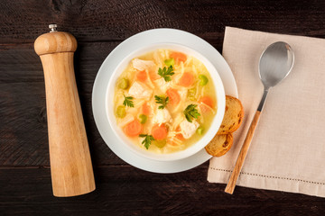 Chicken noodle soup, shot from above on a dark rustic wooden background with toasted bread and a...