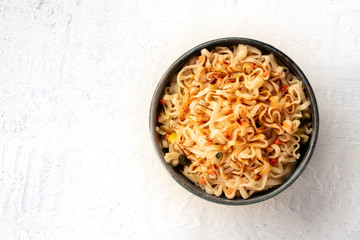 Instant noodles with carrot, scallions, and a dark sauce, shot from the top on a white table with a...