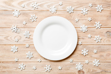 Top view of empty plate surrounded with snowflakes on wooden background. New Year dinner concept