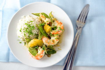 fried tiger prawn shrimp dish with sugar peas, onion, oranges and rice, high angle view from above,...