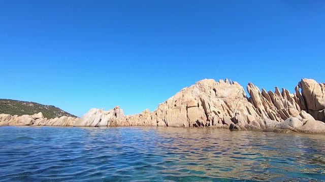 Shooting at water level of a rocky mass of pink granite typical of Sardinia in the middle of the clear sea and blue sky