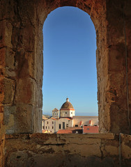 the wonderful dome of the church of San Michele in Alghero city, with its colored majolica, seen through an ancient stone arch