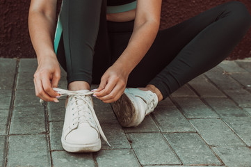 A young girl goes in for sports on the street, tying shoelaces on sneakers.