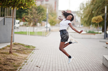 African american dark skinned slim model posed in a black leather shorts and white t-shirt. She jumping at the air.