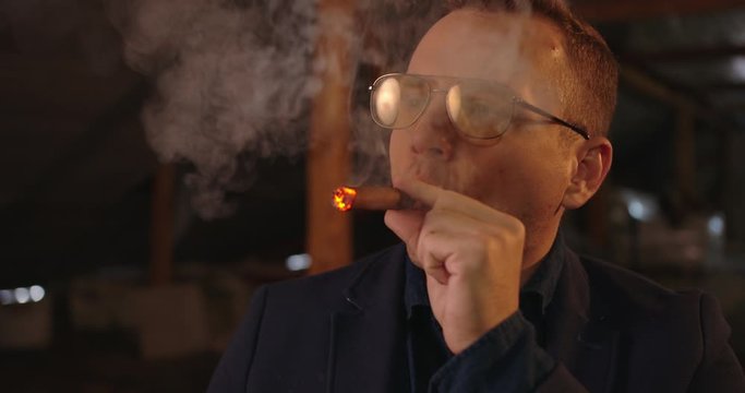 Portrait of handsome elegant man in glasses and blazer , He sets fire his cigare. Dark room location , 