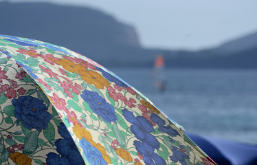 close-up of a colorful decorations of a beach umbrella. The mediterranean sea and a windsurf on the background