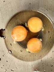 Three raw eggs in a dark glass mug close up