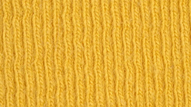 Textile background - yellow cotton fabric with jersey (ribbing) structure. Weave pattern of threads close up. Macro shoot.