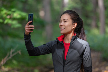 Phone active woman taking picture with mobile cellphone outside on forest nature walk during cardio activity holding smartphone.