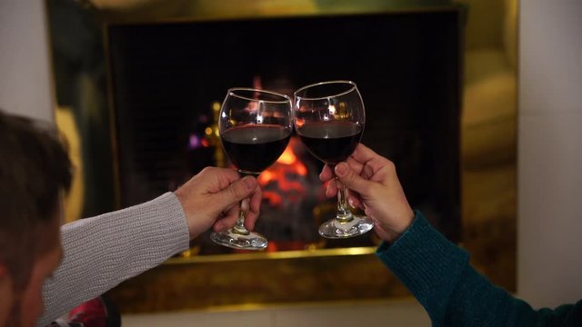 Close up of romantic couplemaking a toast with red wine celebrating happy moments together. Romantic background fireplace in winter holiday vacation, Christmas, valantine or anniversary.