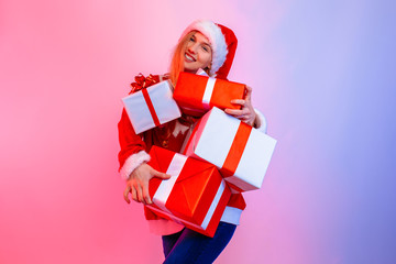 Happy excited young woman wearing Santa hat holding many boxes standing on background