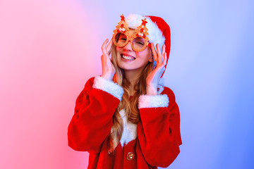 Happy young woman wearing Santa Claus hat standing on background