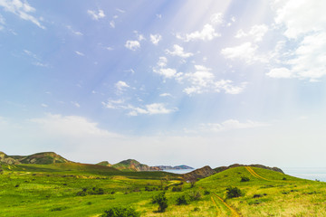 Obraz premium Sunny weather over a field with hills near the sea