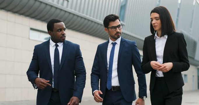 Young multiethnic business team of two men and woman walking the street together and discussing their plans for future or results of work.