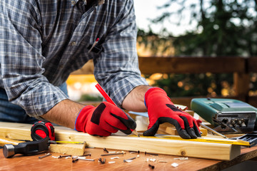 Adult carpenter craftsman wears protective gloves, with a pencil and the carpenter's square trace the cutting line on a wooden table. Construction industry, housework do it yourself. Stock photography