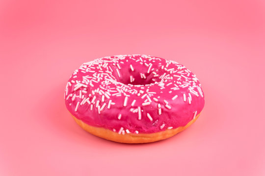A close-up side view of one isolayed pink donut on pink background