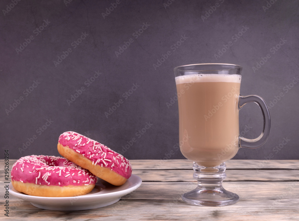 Wall mural A cup of hot coffee and two tasty pink donuts laying in a white small plate on wooden background