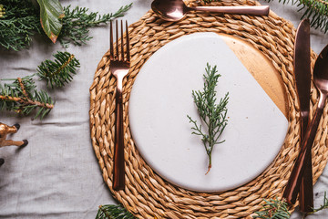 Christmas table settings with a wreath, pine branch and golden cutlery