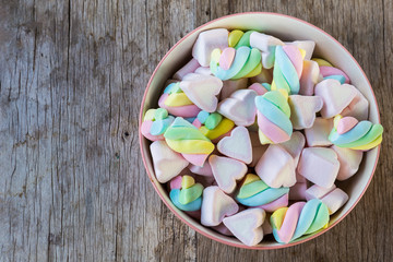 Multi-colored Marshmallow twist and heart in a bowl on a wooden background. Copy space background and texture