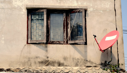 Red satlelite dish on old wall behind windows.
