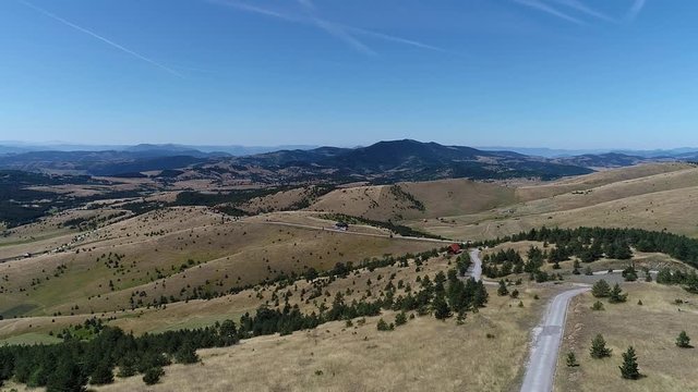 Amazing Countryside Landscape With Meadow, Evergreen Forest, Road and Mountain Peaks on Horizon Aerial