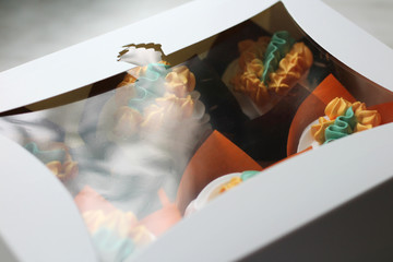 Obraz na płótnie Canvas white cardboard box with a transparent window and multi-colored cupcakes inside
