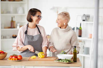 Mother and daughter standing at the table and cooking vegetable salad together in domestic kitchen