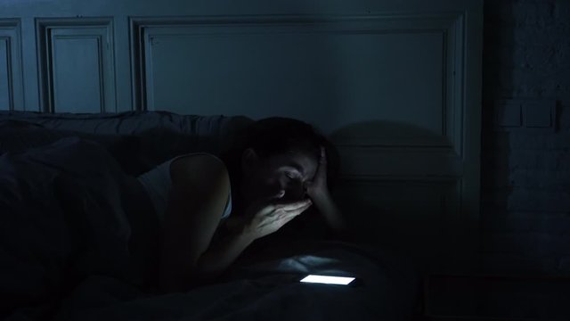 Social media addicted young woman chatting and surfing on the internet using her smart phone sleepy, bored and tired late at night. Dramatic dark light. In Internet, Mobile addiction and insomnia conc