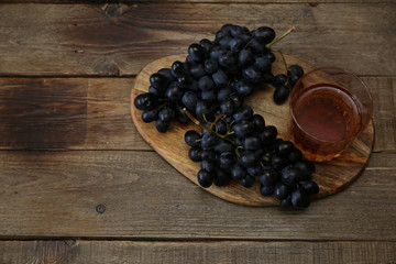 glass of cognac or wine and a juicy bunch of black grapes on a wooden rustic table